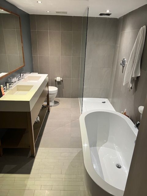 Modern bathroom with a bathtub, dual sinks, toilet, and tiled walls.
