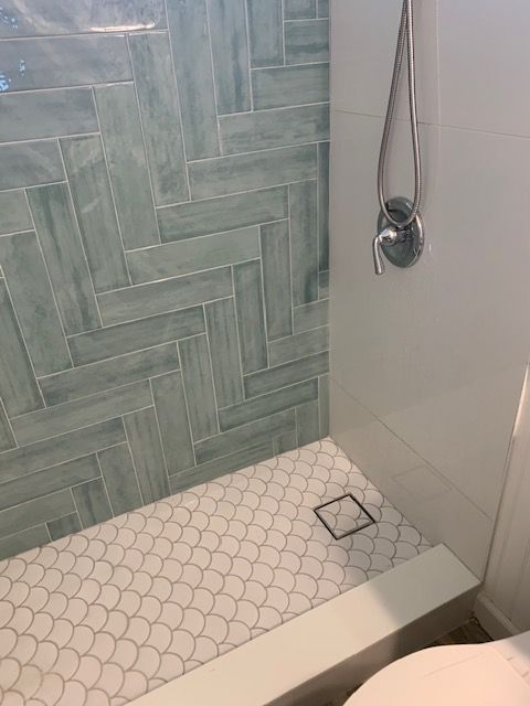 Shower with teal herringbone tile, white fish scale floor tile, and chrome fixtures.
