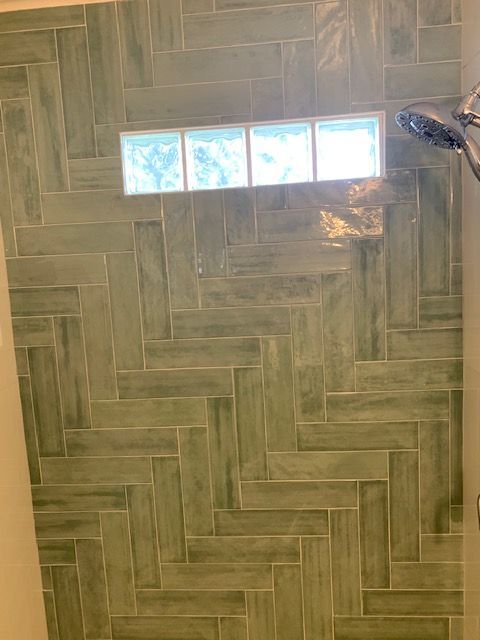 Green herringbone tile shower with glass block window and shower head.