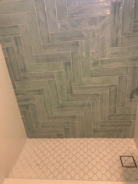 Herringbone-patterned teal tile wall above a floor with white scalloped tiles; a drain visible.