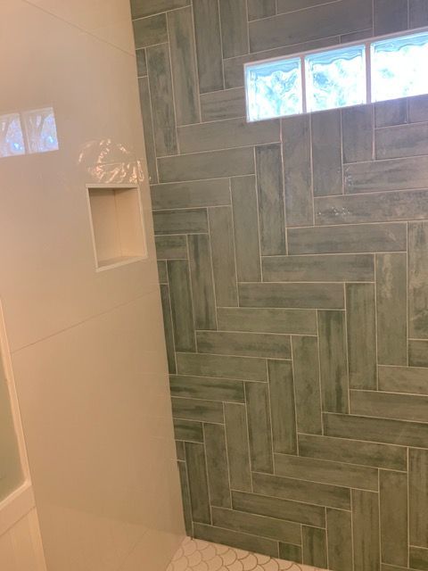 Shower wall with green herringbone tile, a recessed shelf, and glass block window.