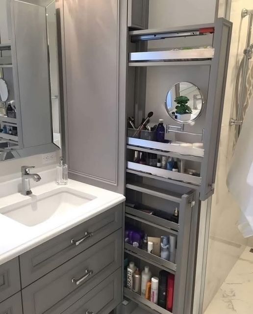 Gray bathroom with open pull-out cabinet stocked with toiletries, beside a vanity with sink and mirror.