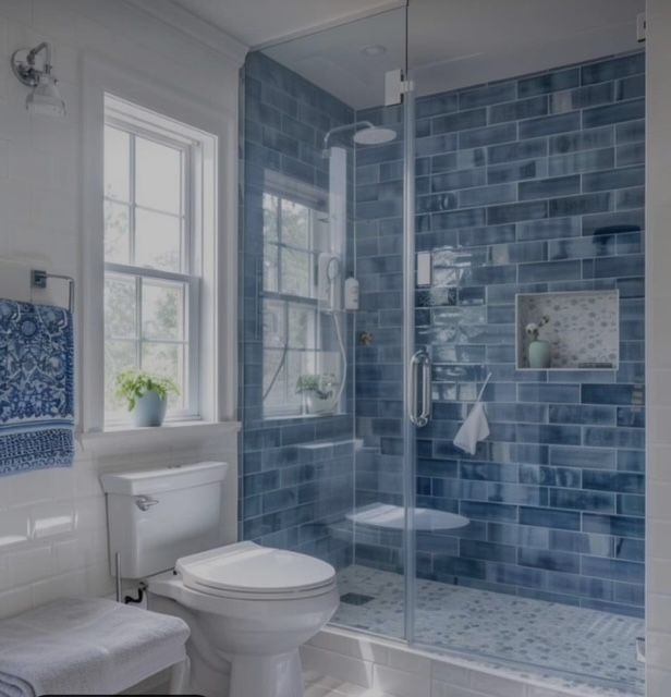 Blue-tiled bathroom with shower, toilet, window, and white accents; towels and plant add decor.
