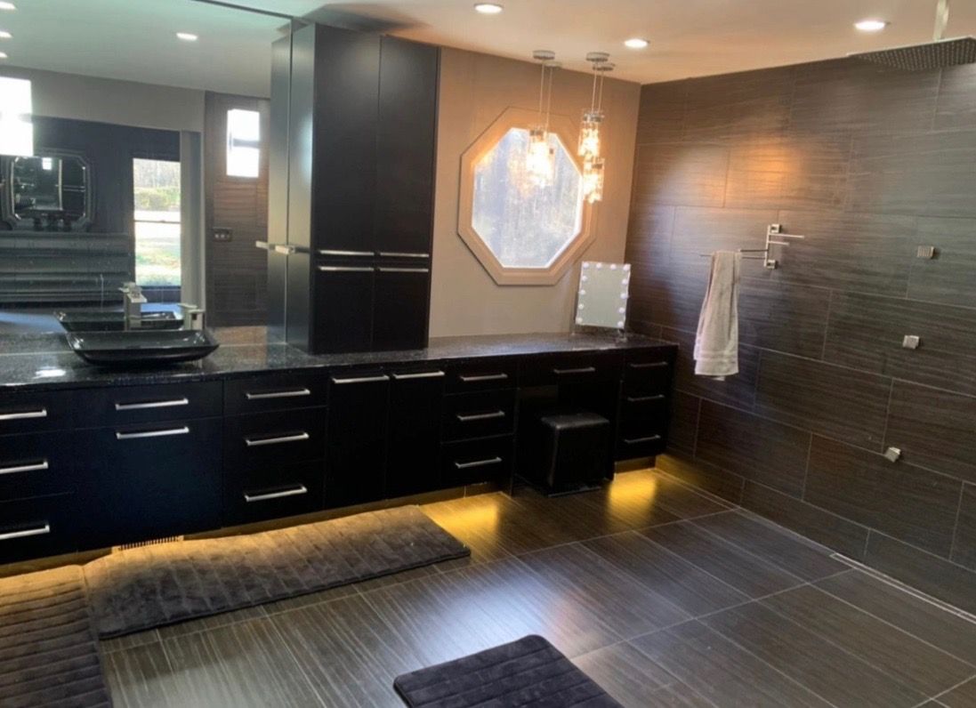 Modern bathroom with dark cabinetry, tile walls and floor, and an octagonal mirror.