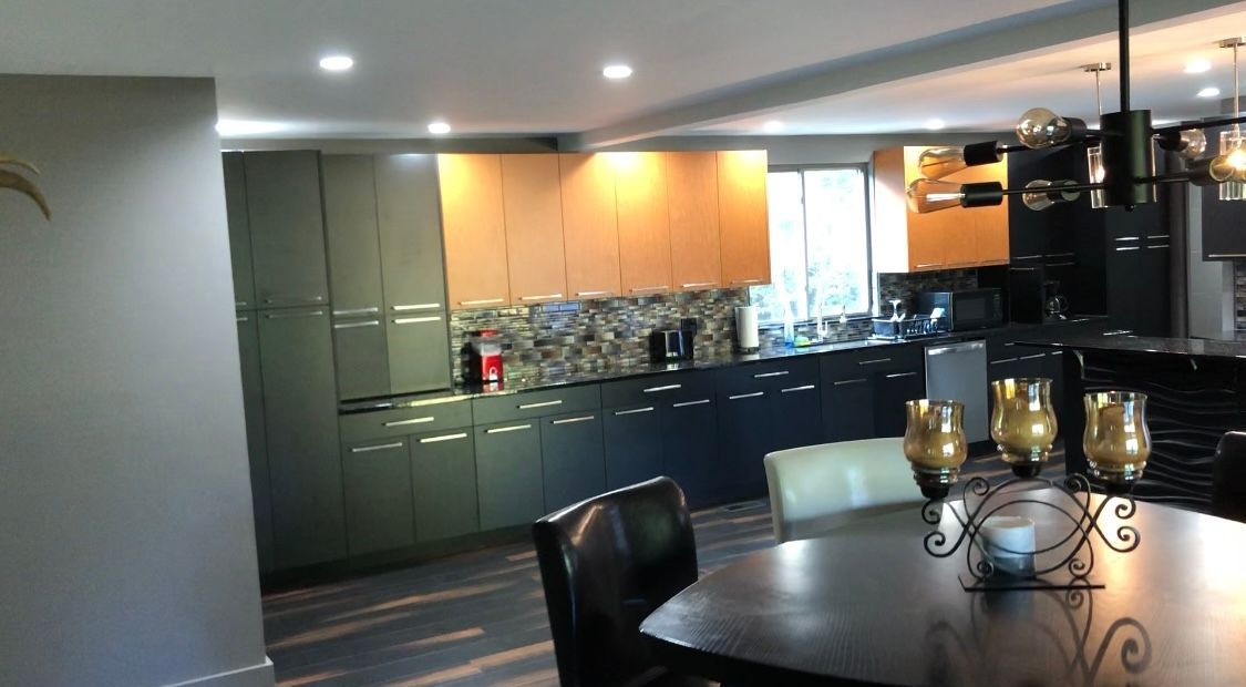Modern kitchen with dark green and tan cabinets, dark countertops, and a dining table.