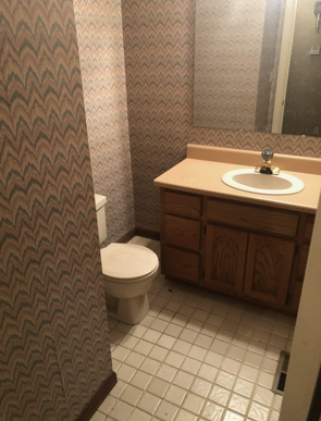 Small bathroom with patterned wallpaper, toilet, sink, and wood vanity.
