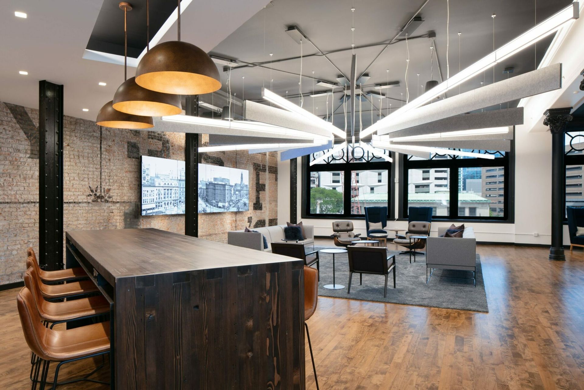 Modern office interior with wooden floors, bar seating, lounge area, and abstract lighting fixtures.
