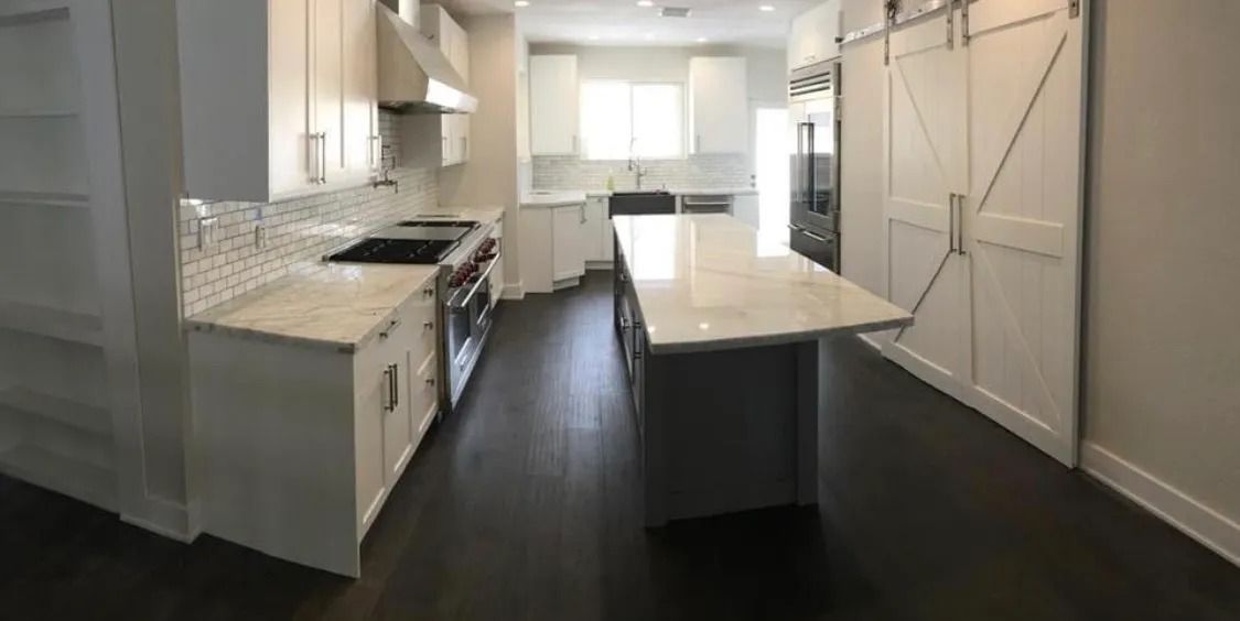 Modern kitchen with white cabinets, island, stainless steel appliances, and dark wood floors.