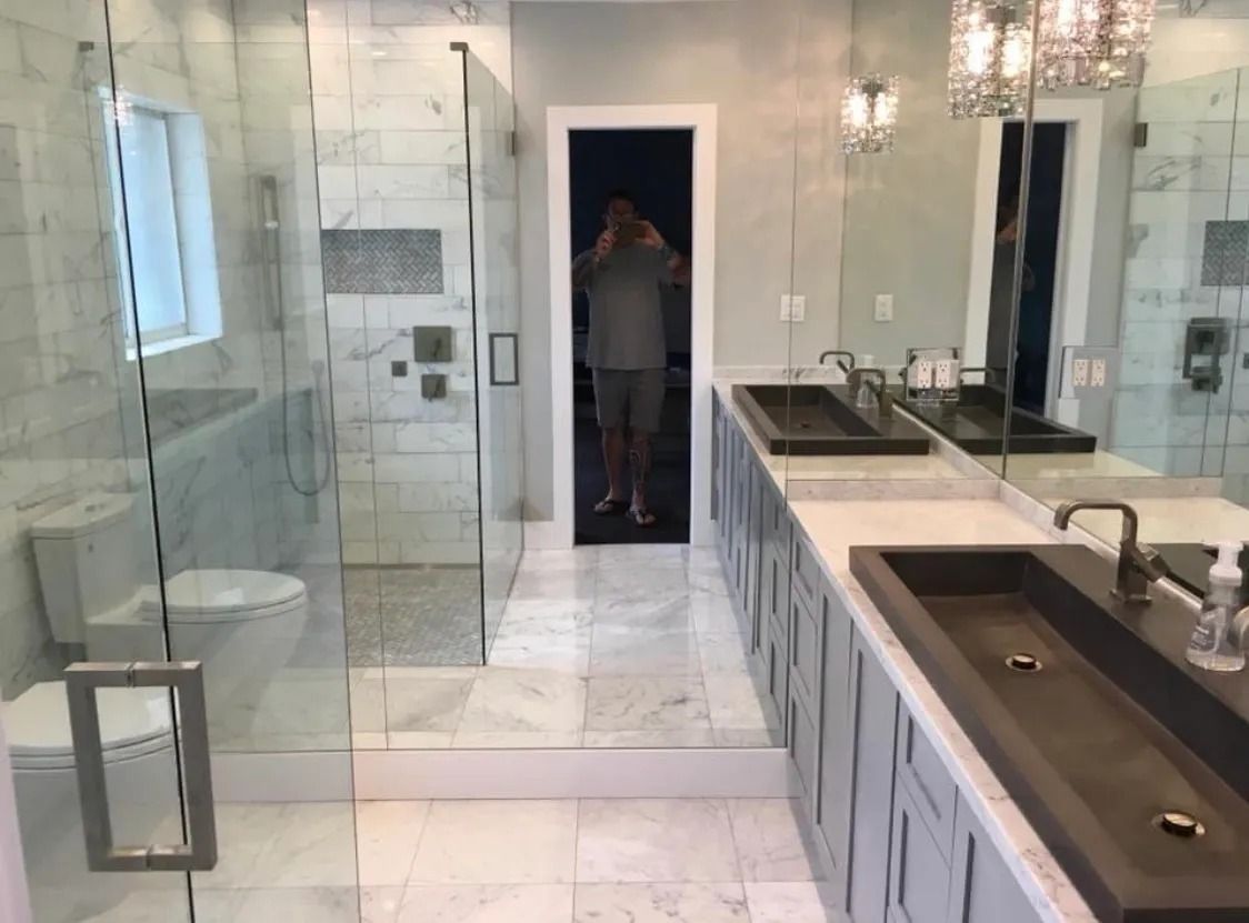 Luxurious bathroom with marble tile, glass shower, double sinks, and a person in the doorway.
