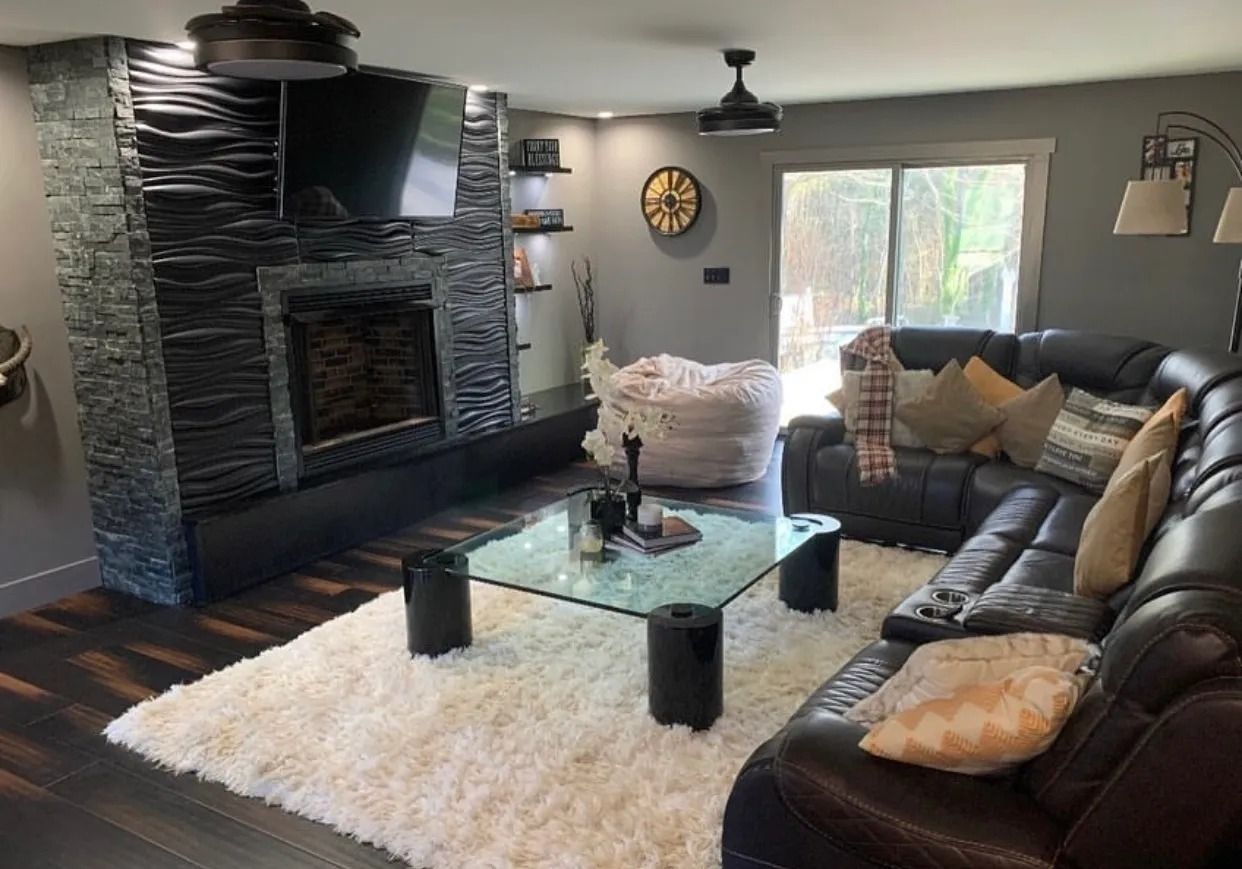 Living room with black leather sectional, fireplace, fluffy white rug, and glass coffee table.