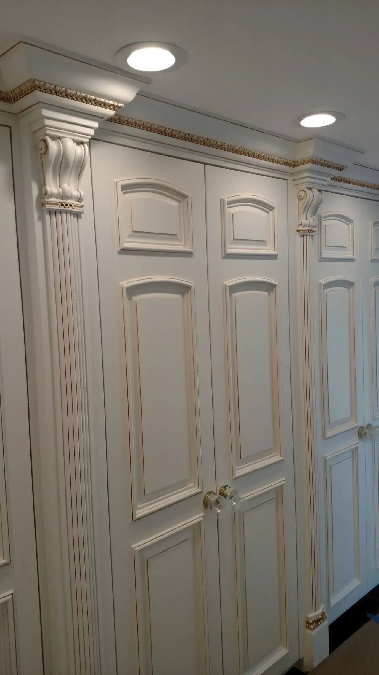 White and gold cabinets with distressed finish, featuring decorative molding and recessed lighting.