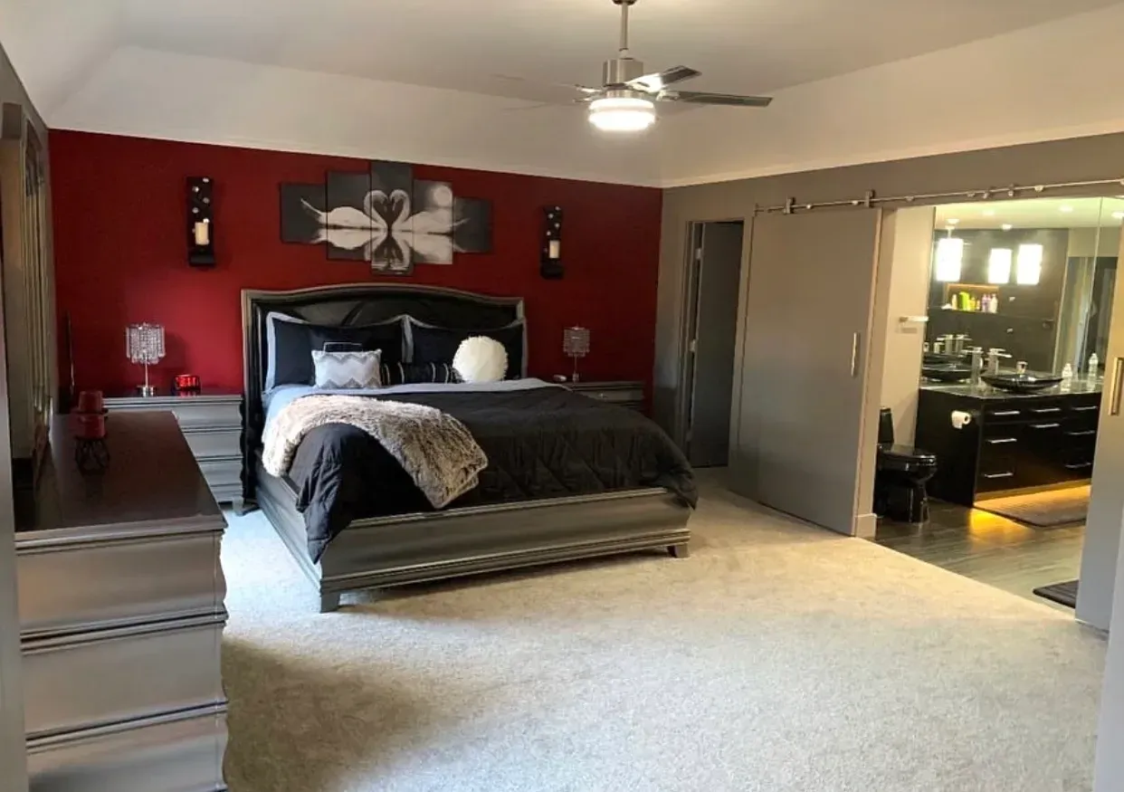 Bedroom with gray bed, red accent wall, sliding door to bathroom.