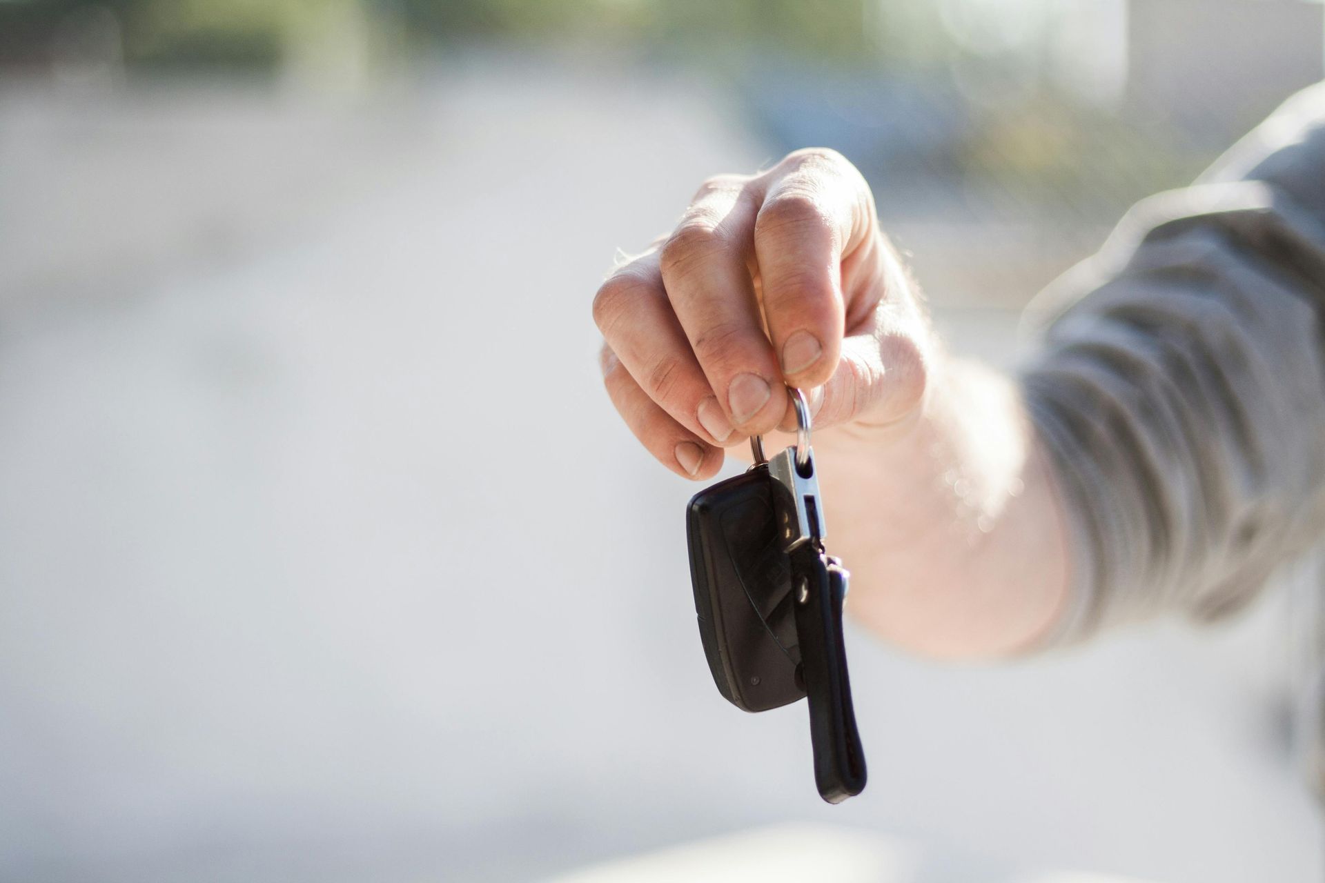A hand holding up a pair of car keys against a blurred outdoor background.