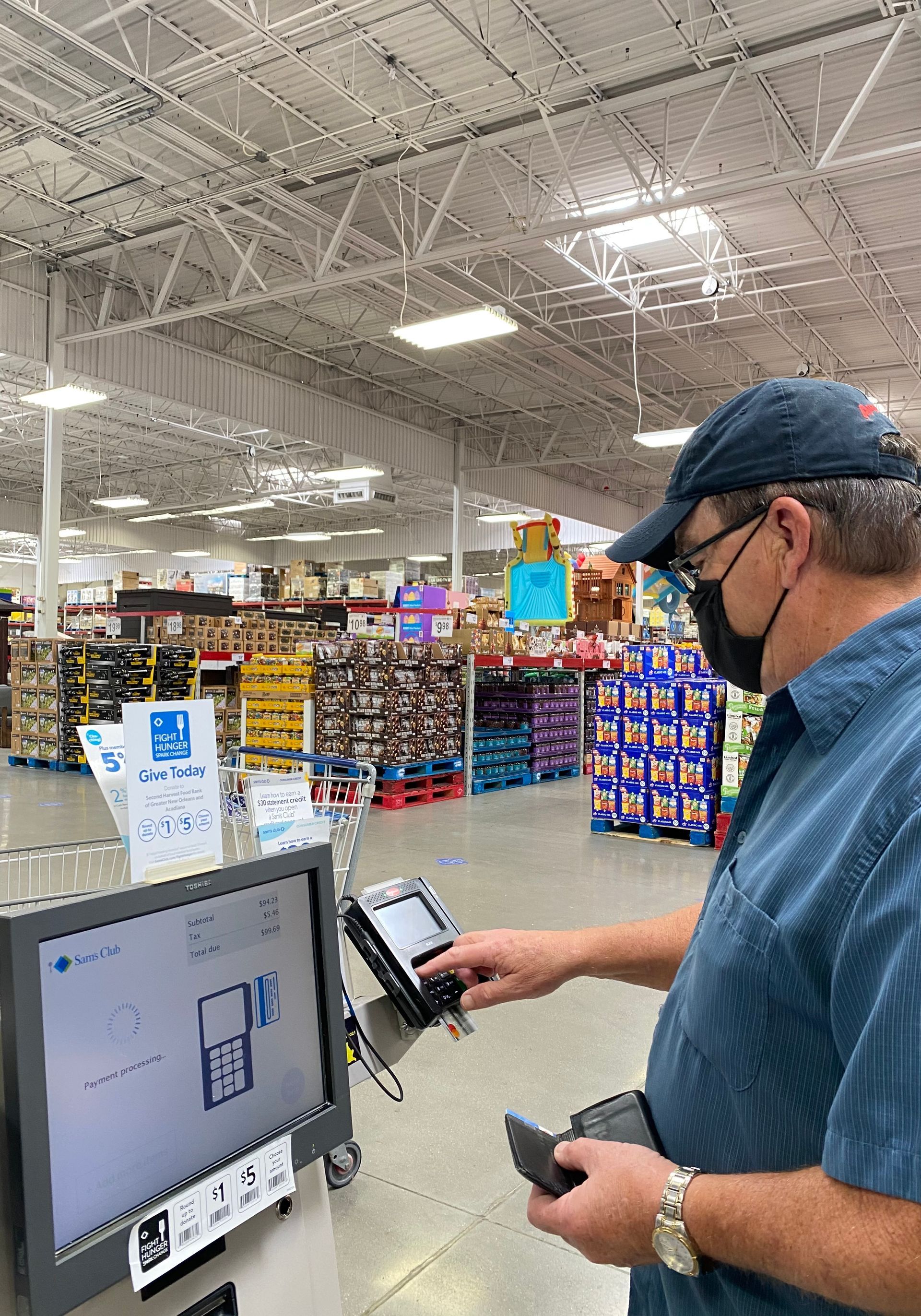 A person wearing a face mask uses a self-checkout terminal in a large retail warehouse store.