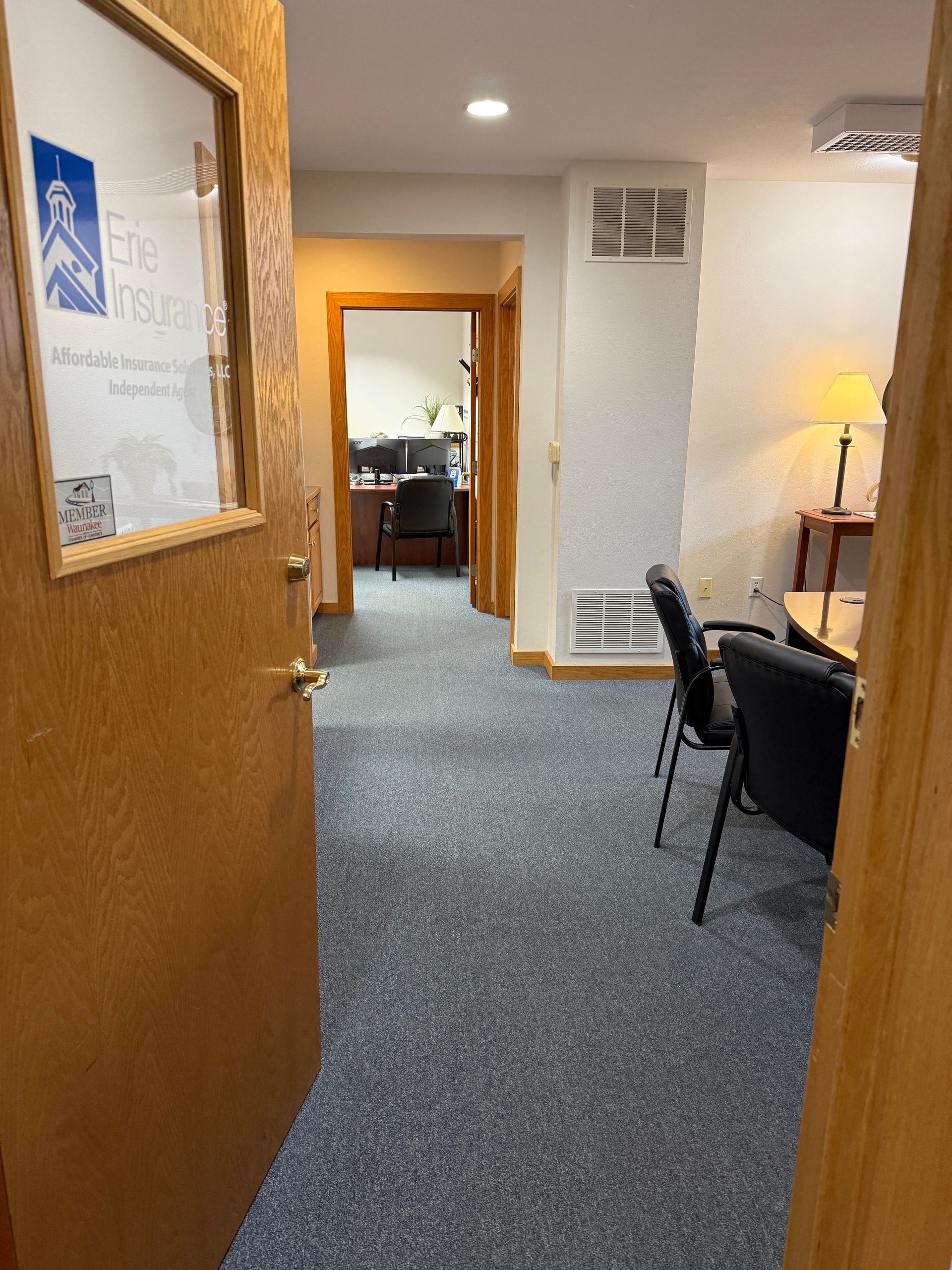 A view from a doorway into an office space with grey carpet, a conference table with black chairs, and an open inner room.