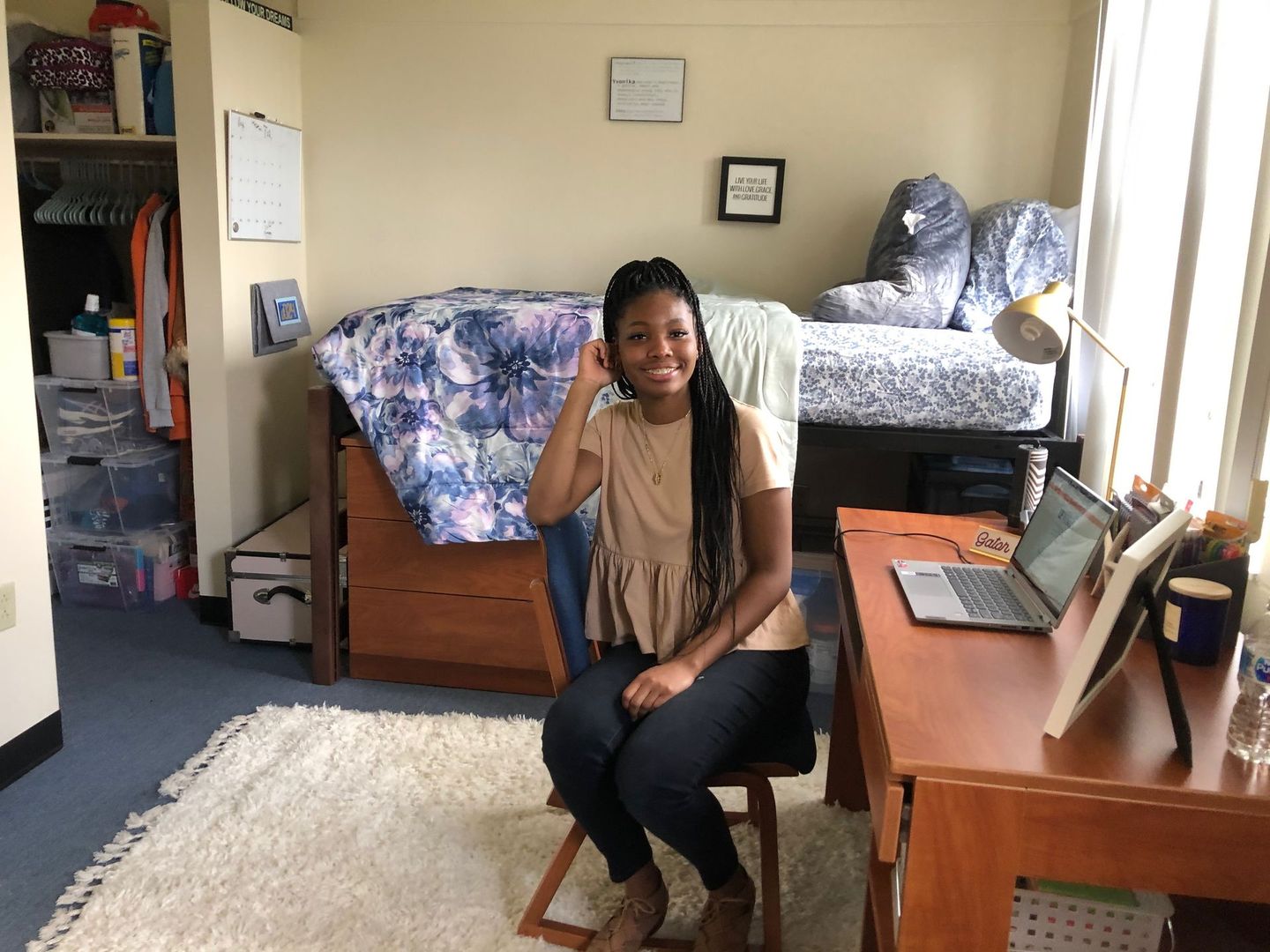 A woman is sitting at a desk in a dorm room.