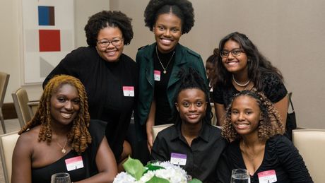 A group of young women are posing for a picture while sitting at a table.