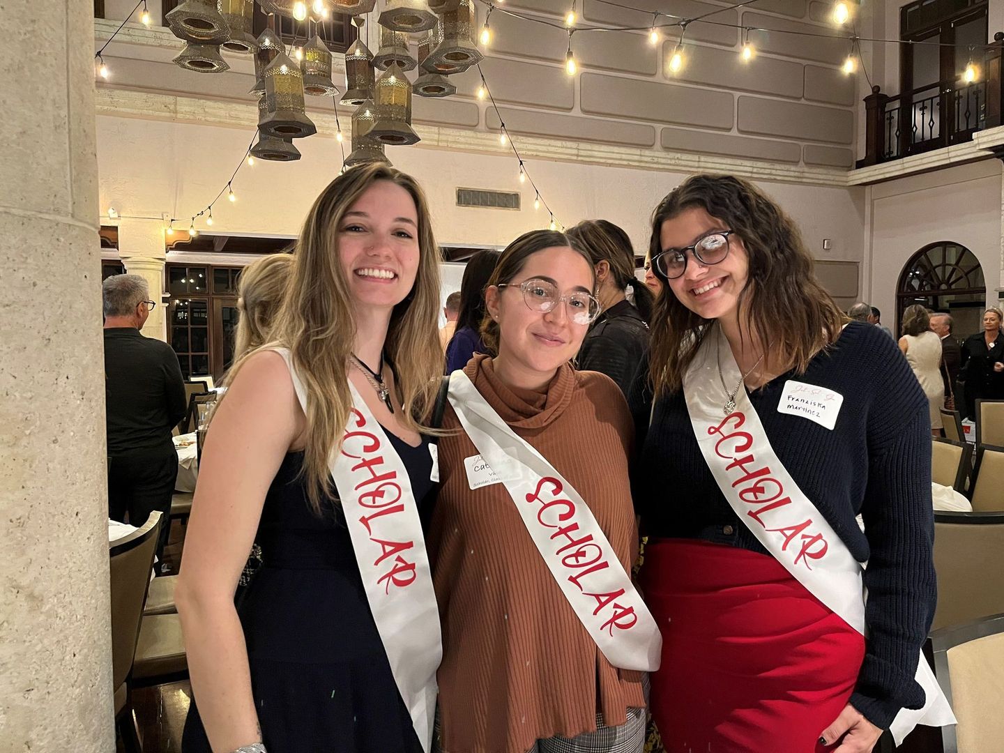 Three women wearing sashes that say scholarship are posing for a picture.