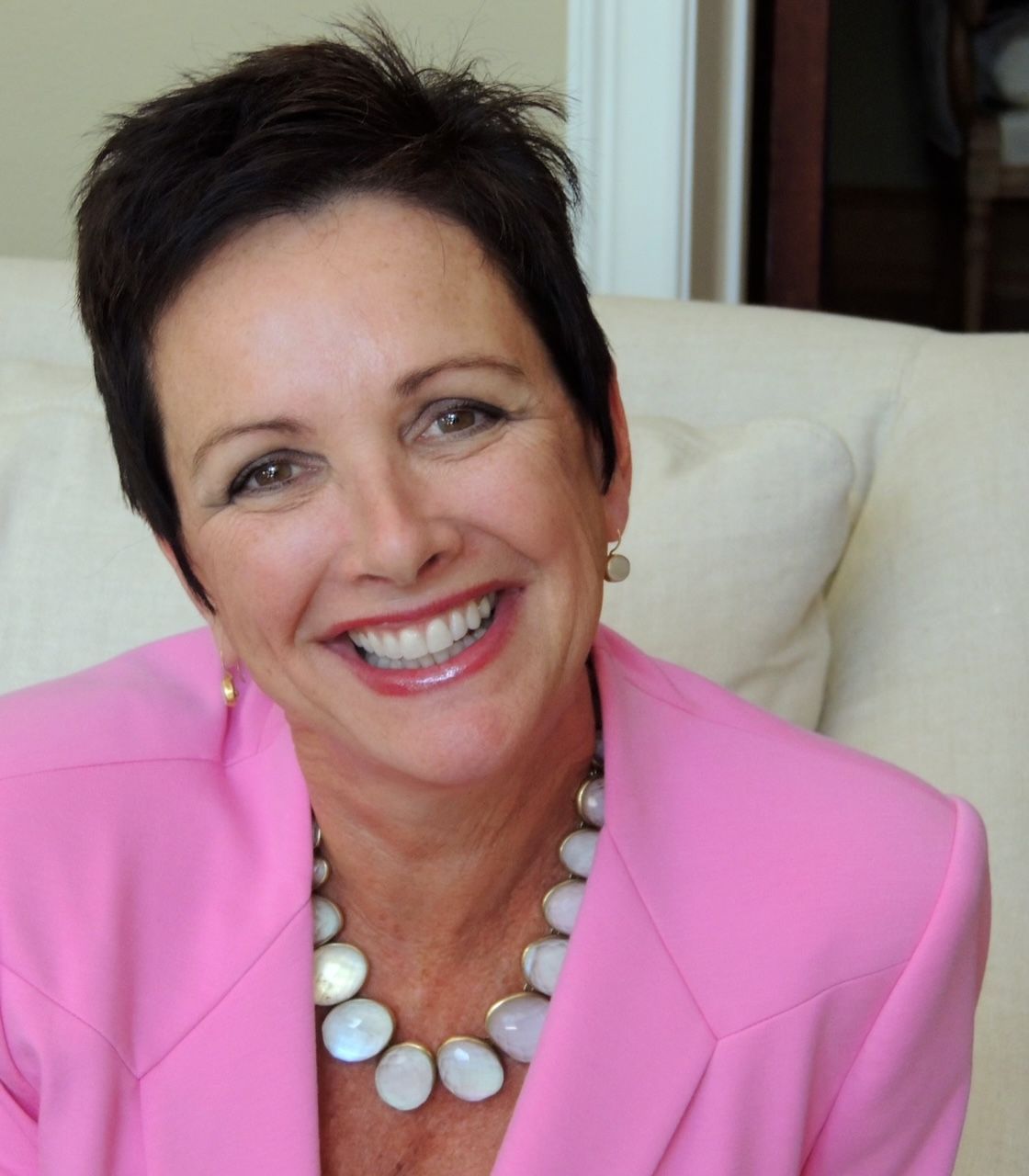 A woman in a pink jacket and necklace smiles for the camera