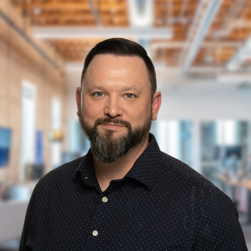 A man with a beard is wearing a blue shirt and standing in a room.