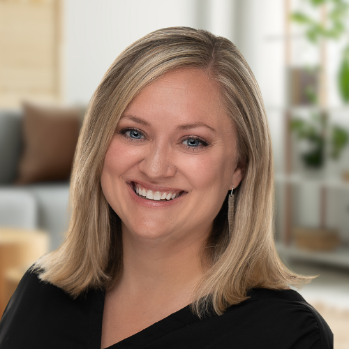 A woman in a black shirt is smiling for the camera in a living room.