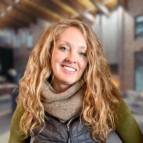 A woman wearing a vest and scarf is smiling for the camera