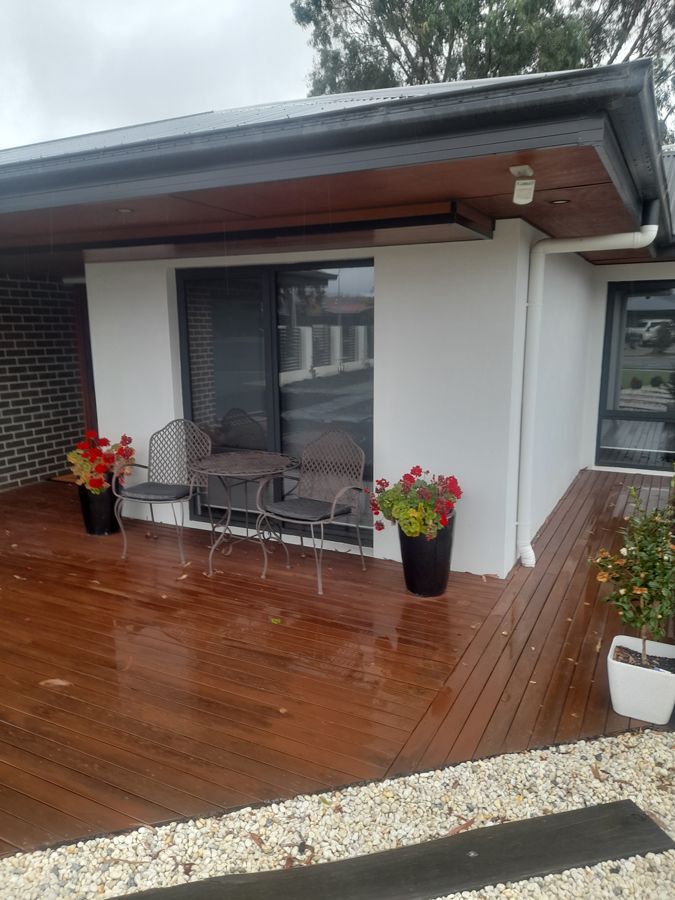 Wooden deck with outdoor furniture, potted red flowers, and a sliding glass door.