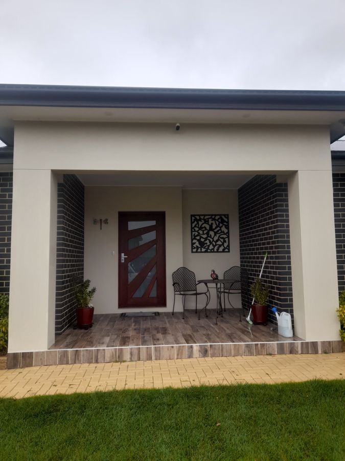 Beige and brick entry porch with a brown door, metal furniture, and a decorative wall hanging.