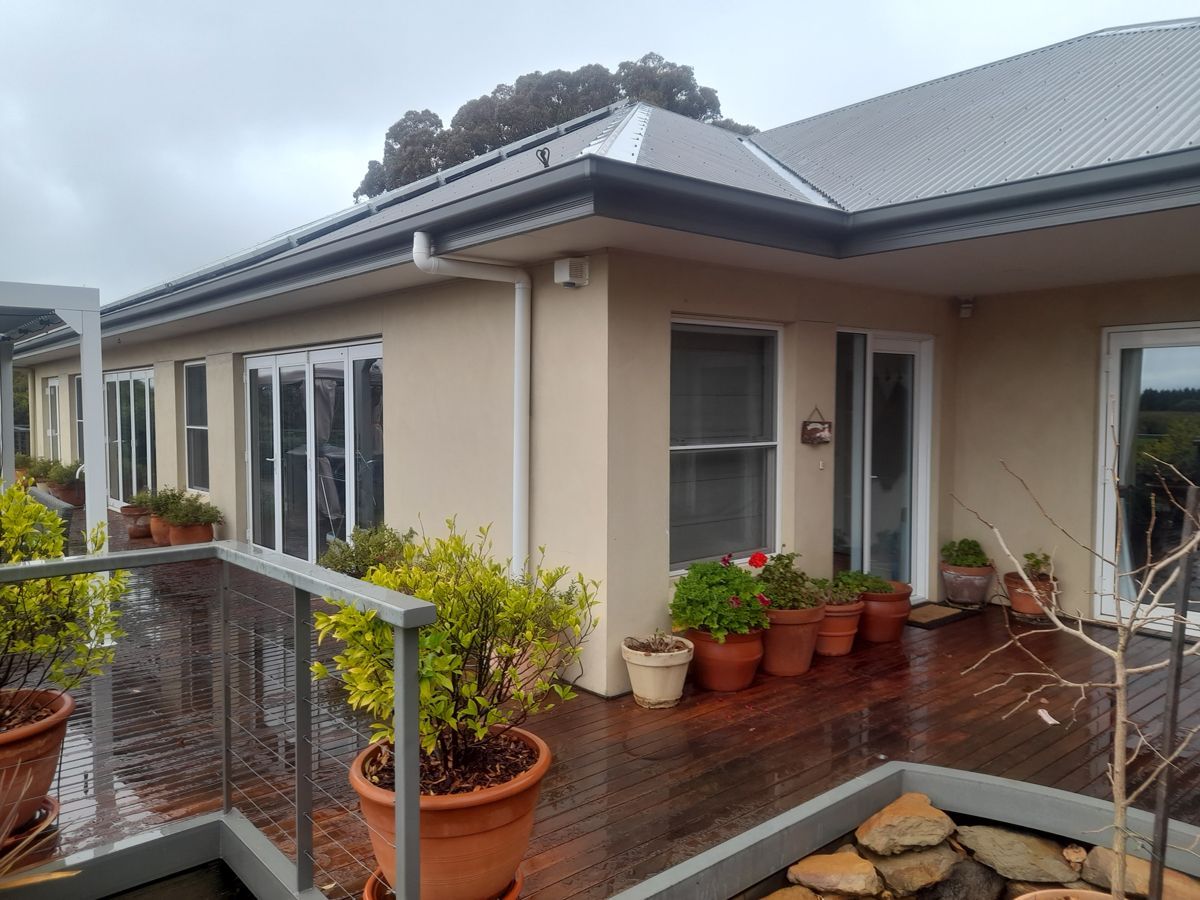 Beige house with a wooden deck, potted plants, and sliding glass doors under a cloudy sky.