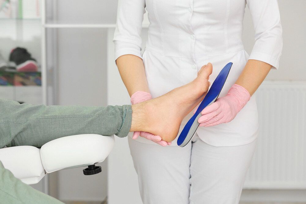 A Woman Is Holding A Blue Insole On A Patient's Foot — Lake Macquarie Podiatry in Belmont, NSW