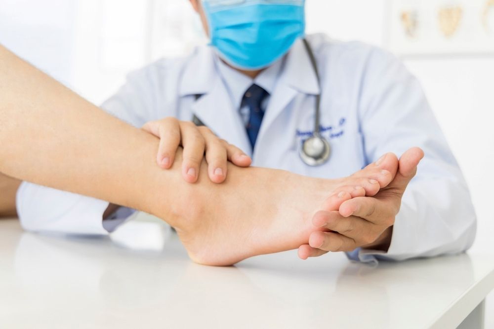 A Doctor Wearing A Mask Is Examining A Patient's Ankle — Lake Macquarie Podiatry in Belmont, NSW