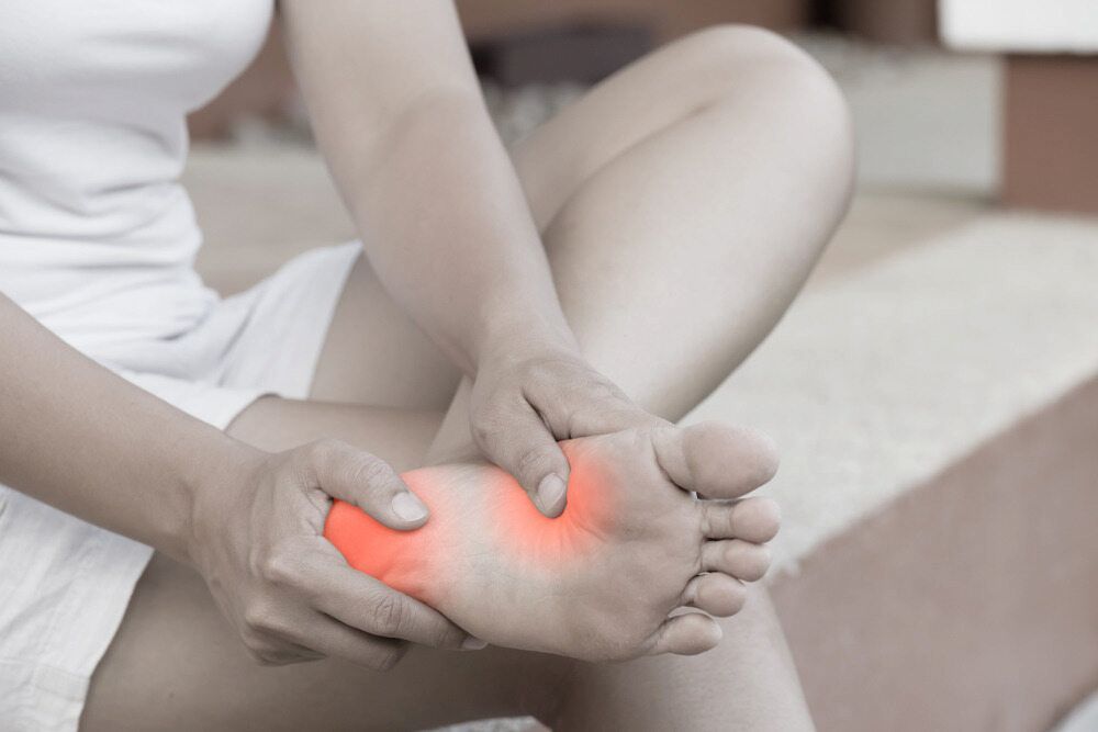A Woman Is Sitting On A Bed Holding Her Foot In Pain — Lake Macquarie Podiatry in Rathmines, NSW