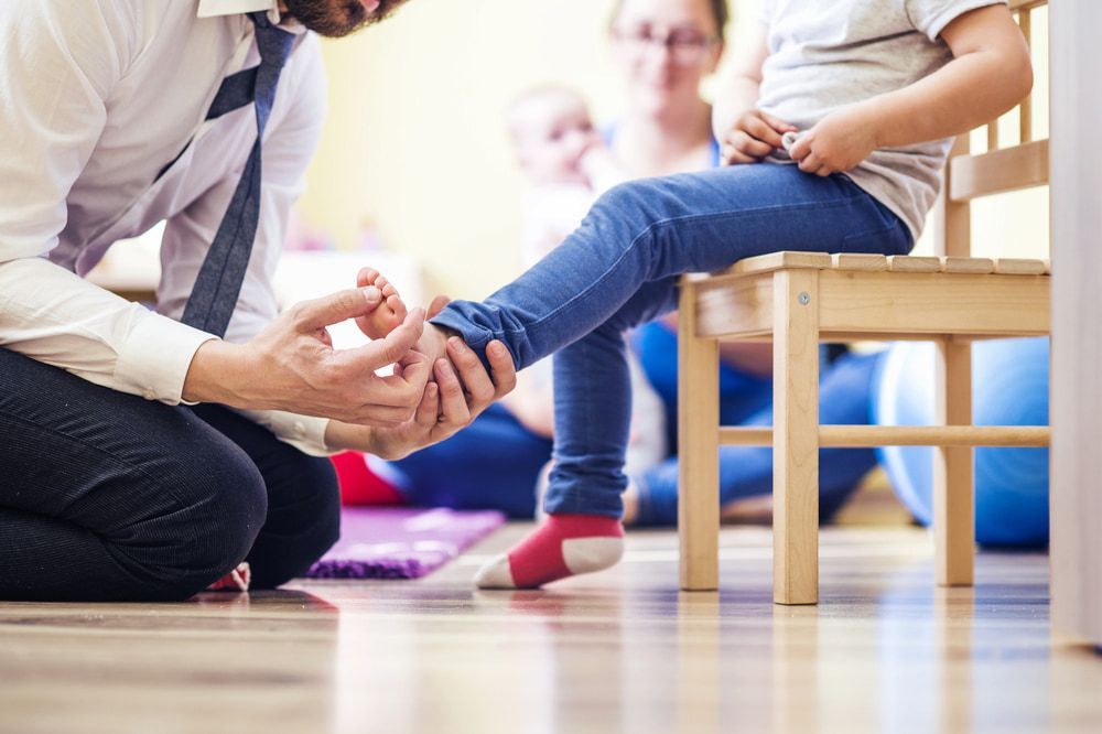 A Man Is Kneeling Down To Help A Little Girl Put On Her Shoes — Lake Macquarie Podiatry in Rathmines, NSW