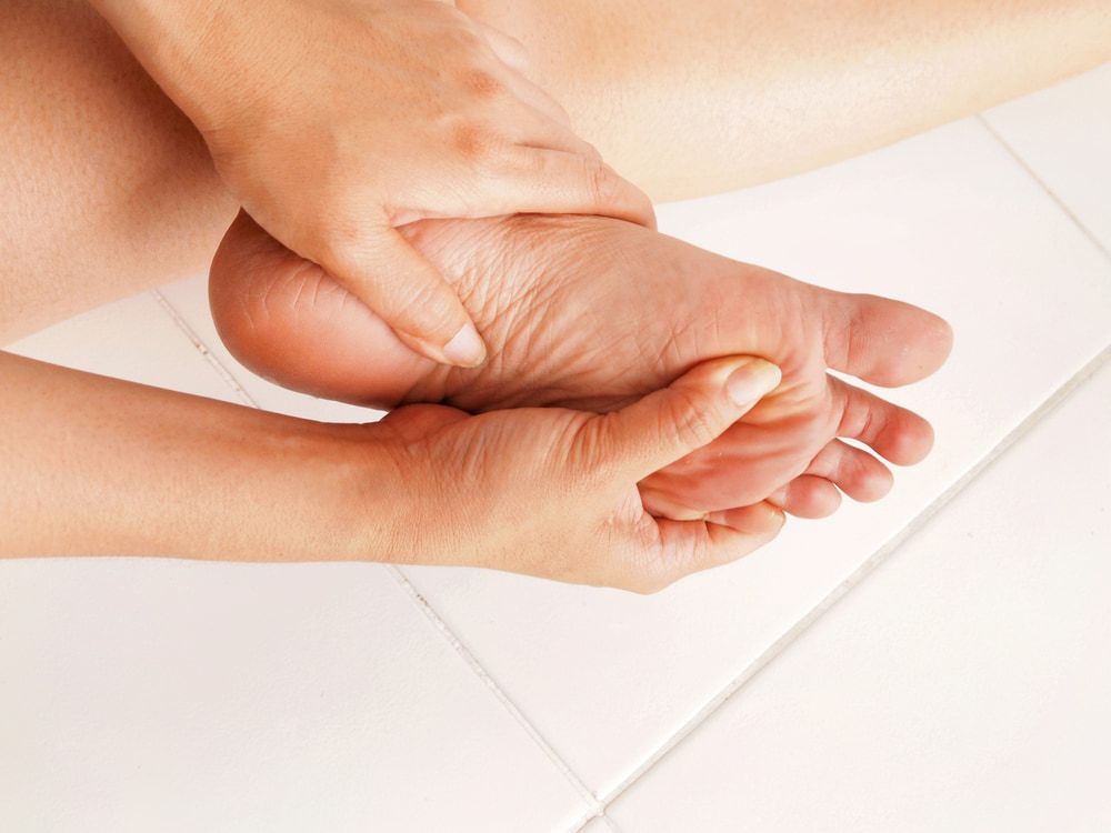 A Person Is Holding Their Foot In Pain On A Tiled Floor — Lake Macquarie Podiatry in Swansea, NSW