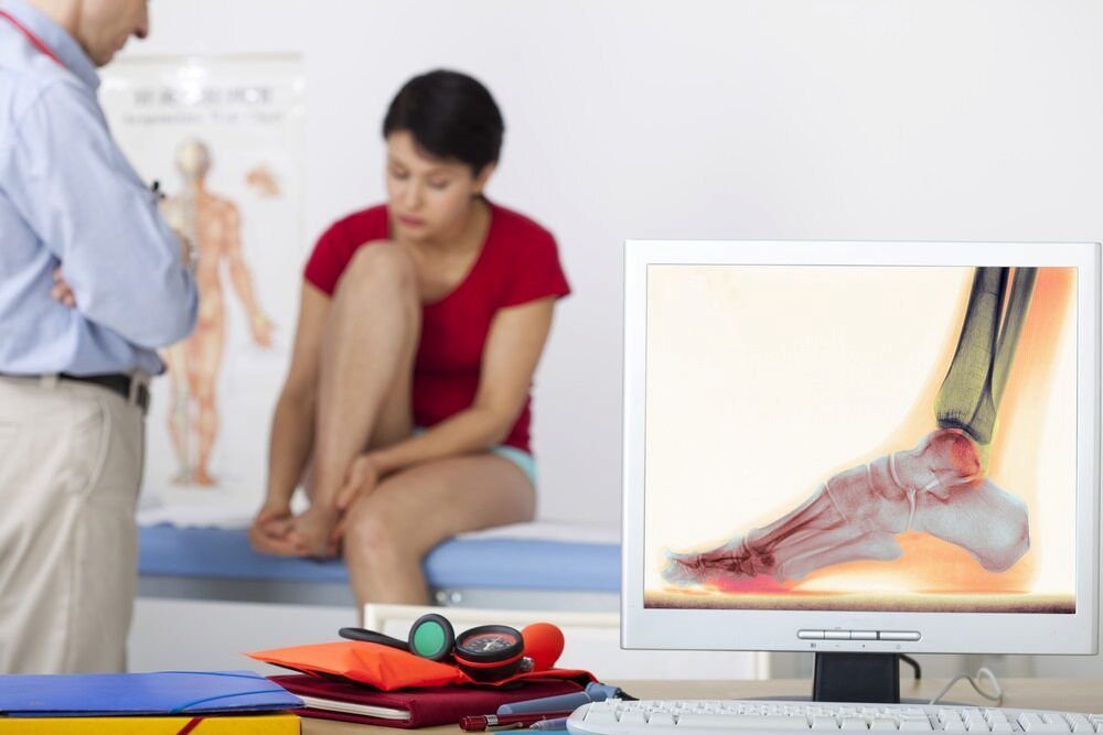 A Woman Is Sitting In Front Of A Computer With A Picture Of Her Foot On It — Lake Macquarie Podiatry in Belmont, NSW