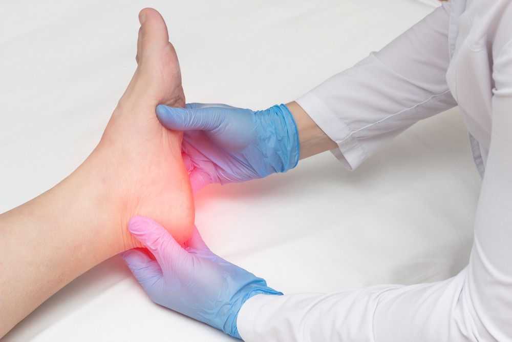 A Doctor Is Examining A Patient's Foot With Blue Gloves — Lake Macquarie Podiatry in Belmont, NSW