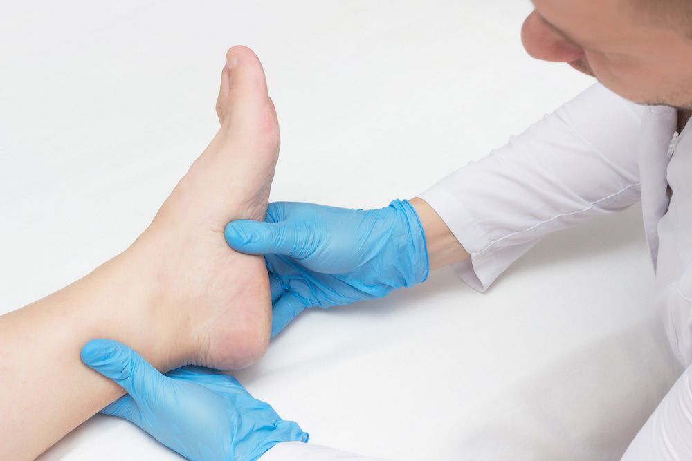 A Doctor Is Examining A Patient's Foot With Blue Gloves — Lake Macquarie Podiatry in Rathmines, NSW