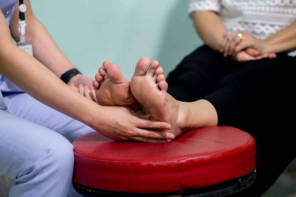 A Nurse Is Massaging A Patient's Feet On A Red Stool — Lake Macquarie Podiatry in Belmont, NSW