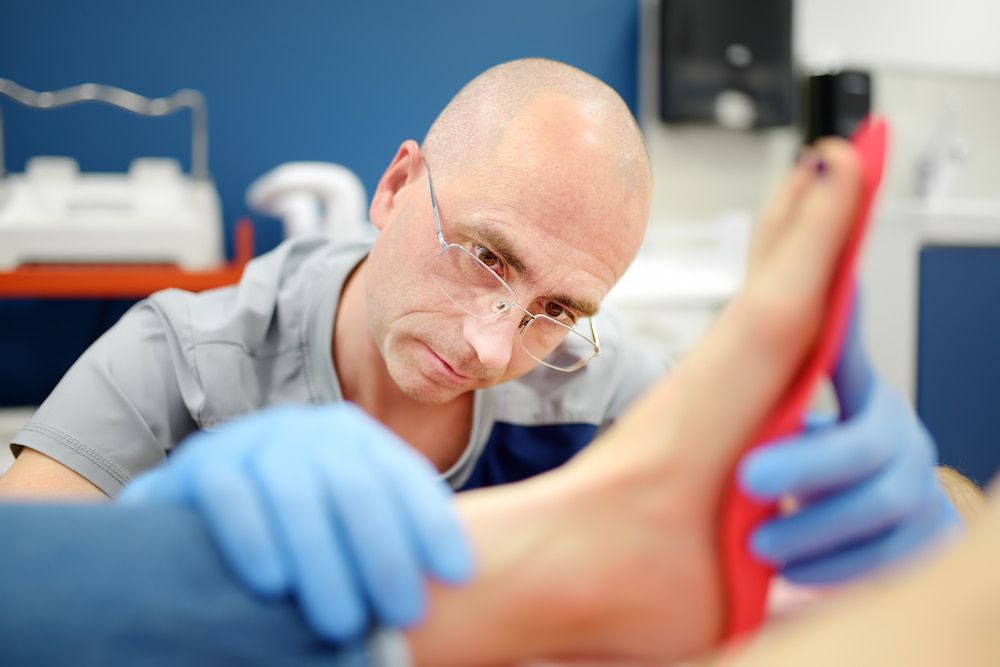 A Man Is Examining A Person's Foot In A Hospital — Lake Macquarie Podiatry in Swansea, NSW