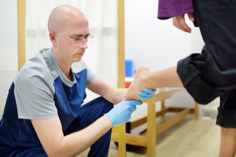 A Doctor Is Examining A Patient's Foot With Blue Gloves — Lake Macquarie Podiatry in Rathmines, NSW