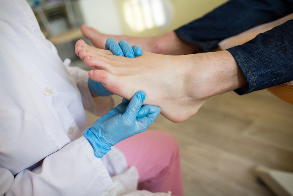 A Doctor Is Examining A Patient's Foot With Blue Gloves — Lake Macquarie Podiatry in Rathmines, NSW