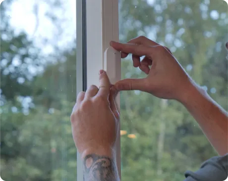 Person's hands adjusting a white window seal next to glass window with trees visible in the background.