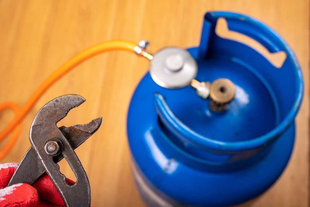 A Person is Holding a Pair of Pliers Next to a Gas Cylinder — Gastech Plumbing Services in Andergrove, QLD
