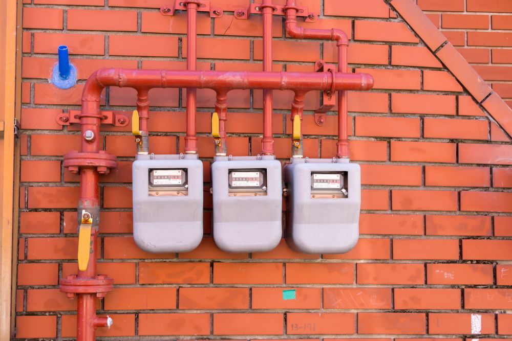 Three Gas Meters Are Hanging on a Brick Wall — Gastech Plumbing Services in Marian, QLD