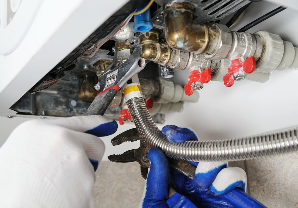 A Person is Fixing a Boiler With a Wrench and Hose — Gastech Plumbing Services in Sarina, QLD