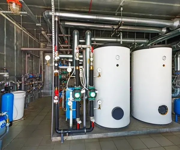 Two Water Heaters Are Sitting Next to Each Other in a Room With Pipes — Gastech Plumbing Services in Andergrove, QLD