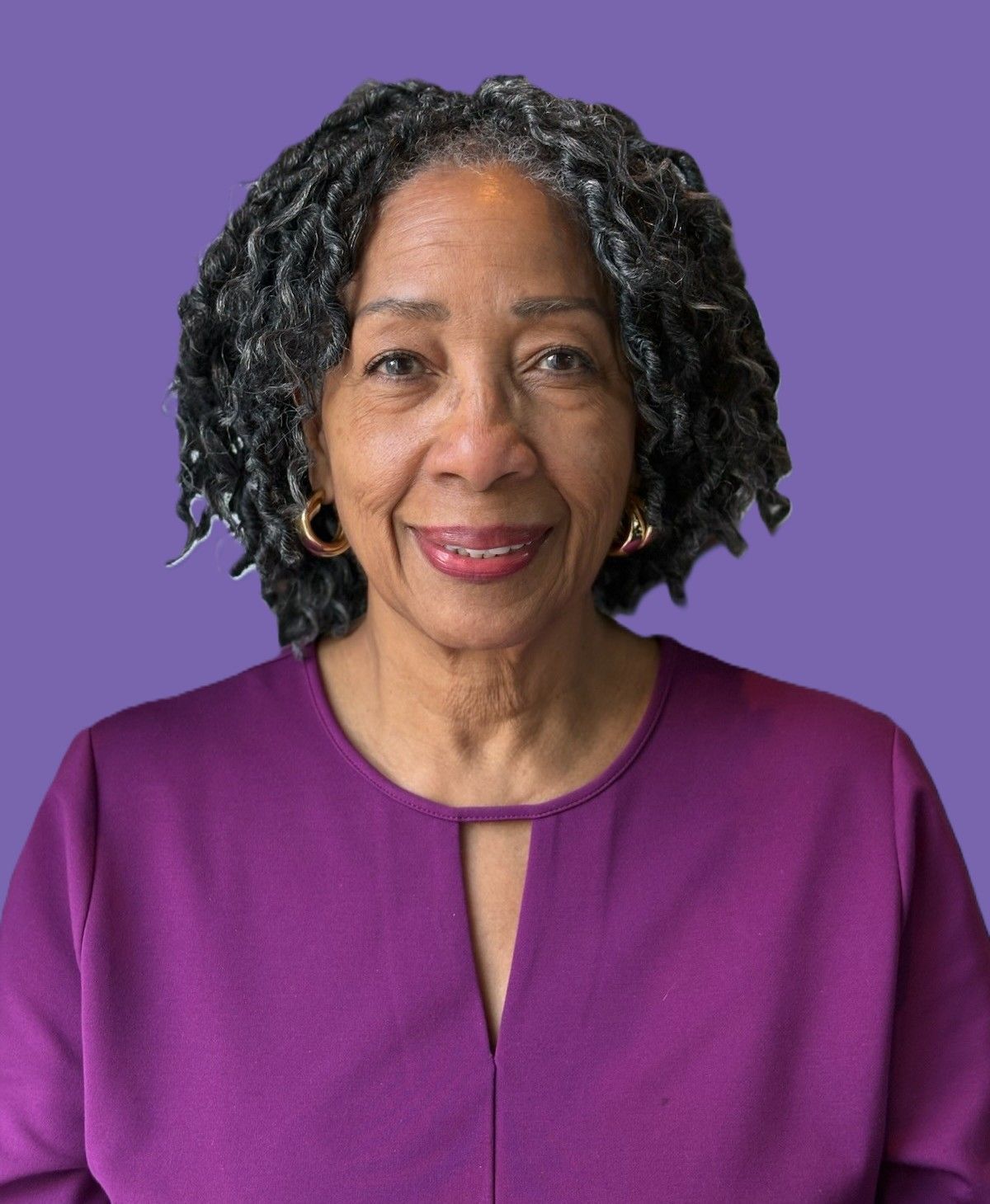 A woman with dreadlocks is wearing a purple shirt and earrings.
