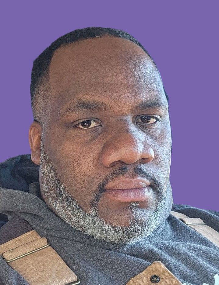 A man with a beard is sitting in front of a purple background.