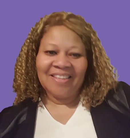 A woman with curly hair is smiling and wearing a white shirt and a black jacket.
