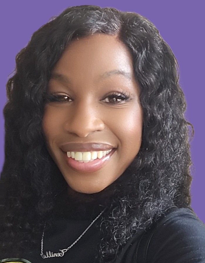 A woman with curly hair is smiling and wearing a necklace.